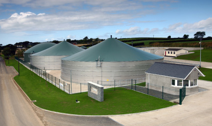 Anaerobic digester tanks with green conical roofs beside landscaped grounds